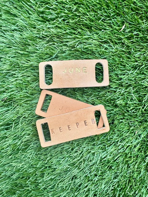 Three leather tags with engraved text on a grass background